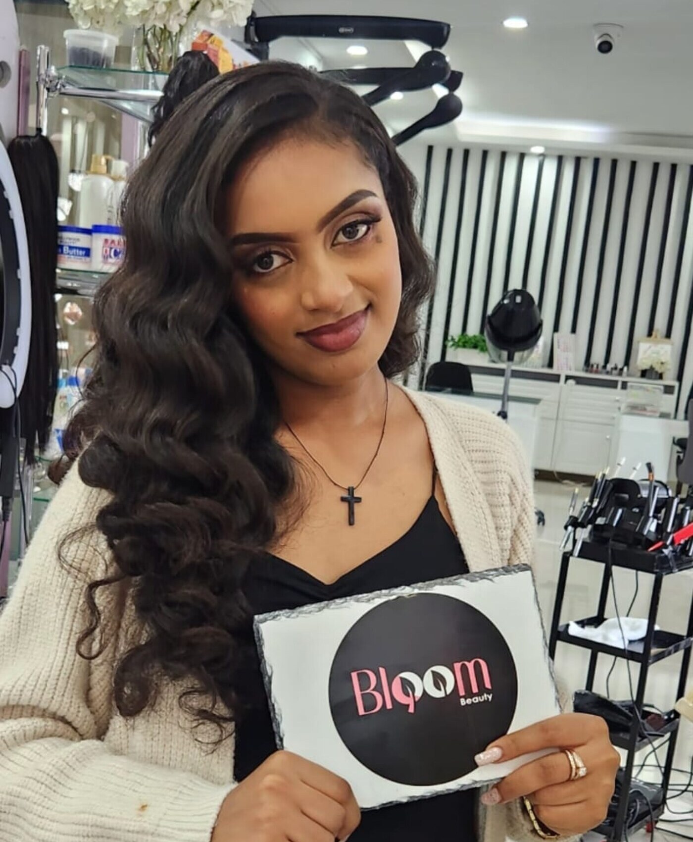 A Bloom Beauty client styled with long curly extensions, holding the Bloom logo in the salon.